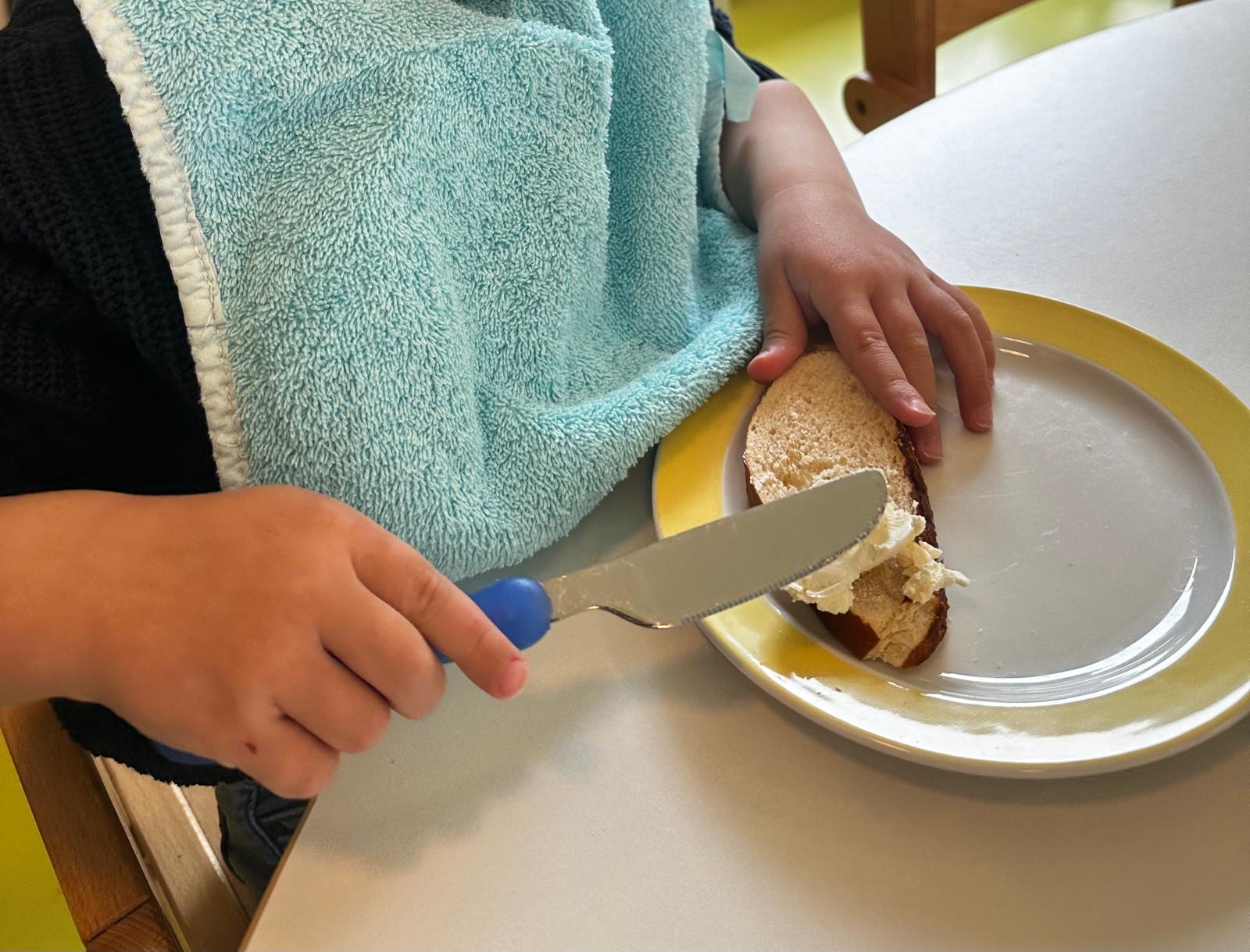 Kind hilft in Solln bei der zubereitung des Frühstücks und schneidet mit kindgerechtem Besteck eine Frucht.